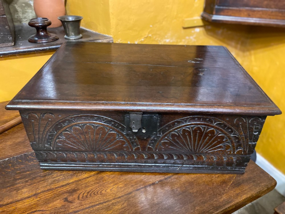 A dark oak wooden bible box featuring a flat hinged top, an iron lock plate, and hand-carved demi-lune fan motifs across the front panel.