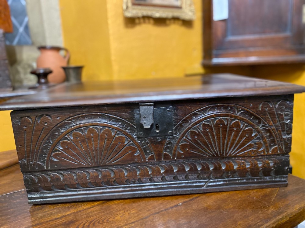 A dark oak wooden bible box featuring a flat hinged top, an iron lock plate, and hand-carved demi-lune fan motifs across the front panel. View II