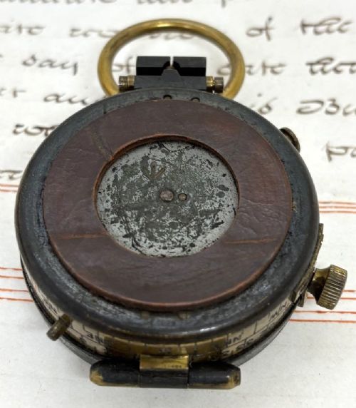 A First World War brass field compass with a patinated brass casing, glass crystal display, and fitted dark brown leather protective case. View VI