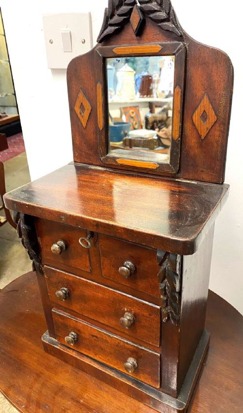 A Victorian miniature mahogany chiffonier featuring a small rectangular mirror, carved leaf cresting, inlaid diamond motifs, and small drawers with turned knobs. View II