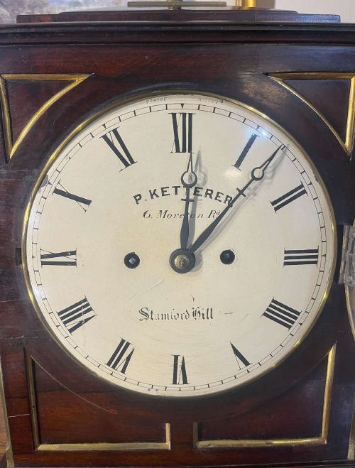 fig 1. A Regency mahogany bracket clock featuring brass corner inlay, a top pineapple finial, brass ball feet, and a cream painted dial signed P. Ketterer Stamford Hill.