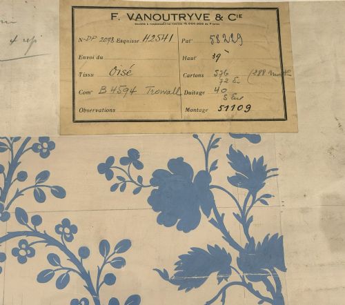 fig 2. A framed vintage French textile design featuring a blue floral motif rendered on grid paper, complete with technical handwritten annotations and an original manufacturer label.