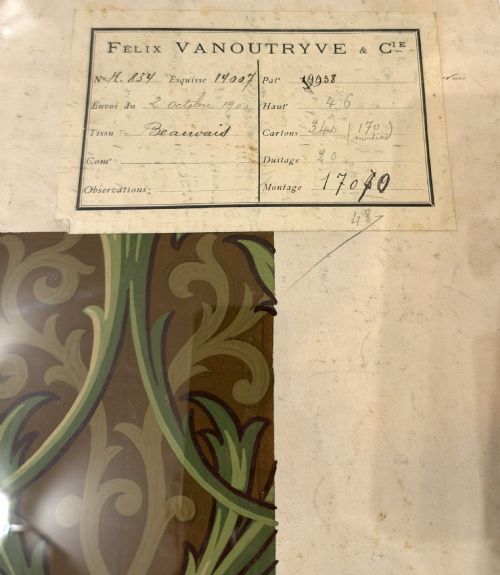 fig 2. A framed antique French textile design on paper featuring stylized green leaves and blue botanical buds against a patterned brown background.