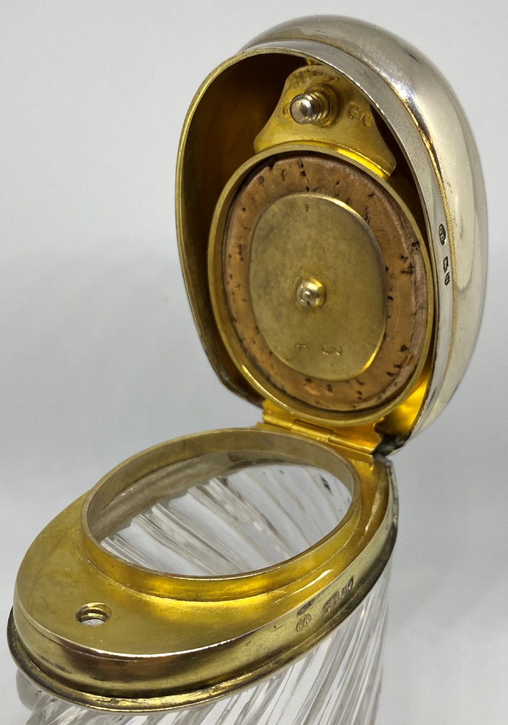 A spiral-cut clear glass cologne bottle featuring a hinged silver lid with a gilt interior and internal locking tab. View V