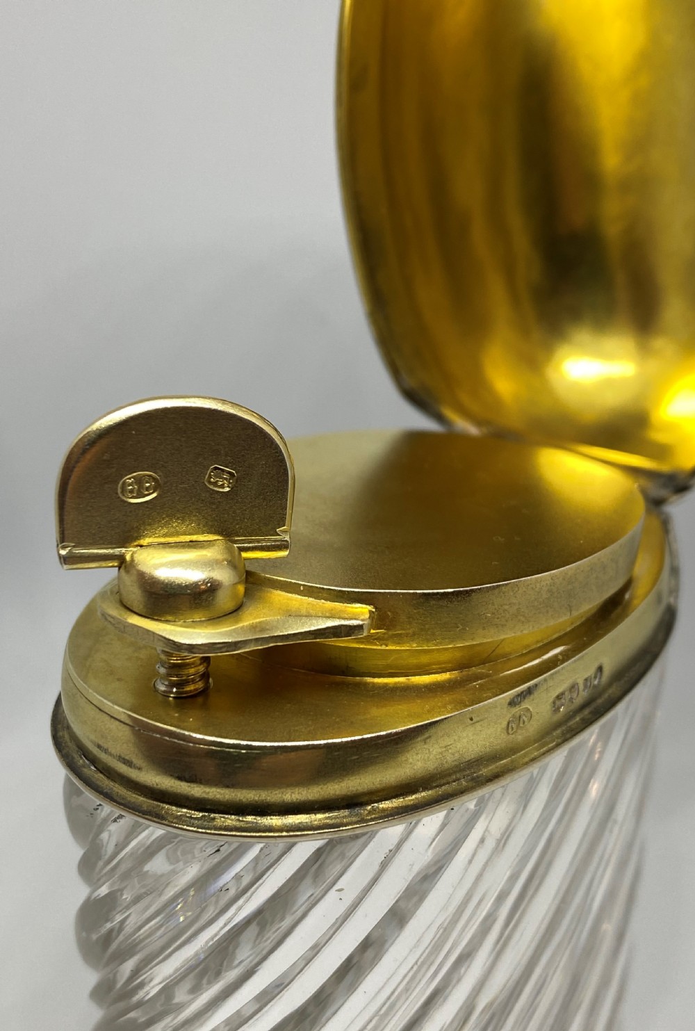 A spiral-cut clear glass cologne bottle featuring a hinged silver lid with a gilt interior and internal locking tab. View VI