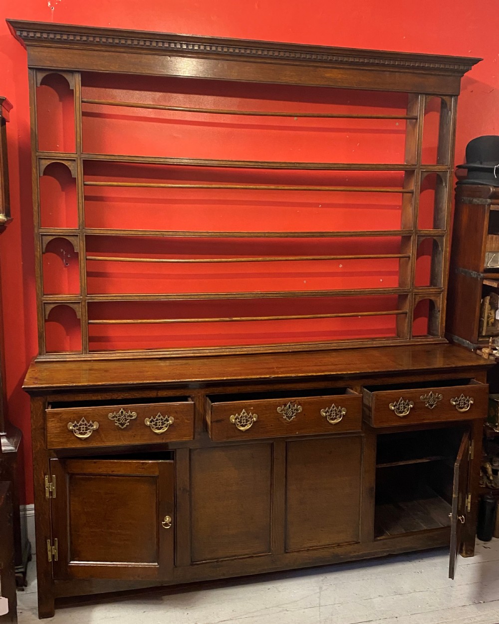 A George III oak dresser featuring an open upper plate rack with slender horizontal rails above three drawers and lower panelled cupboards with brass fittings. View III