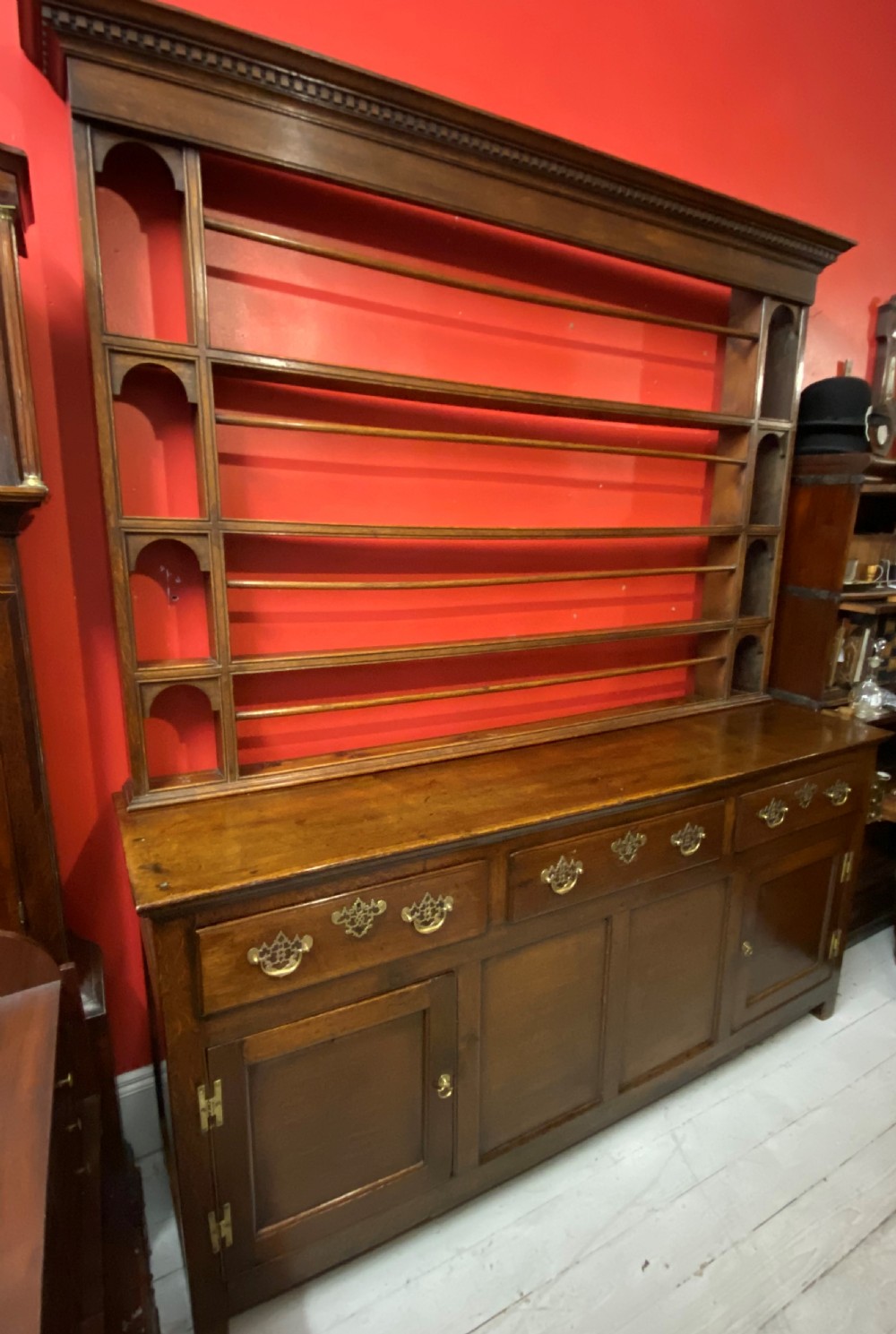 A George III oak dresser featuring an open upper plate rack with slender horizontal rails above three drawers and lower panelled cupboards with brass fittings. View VI