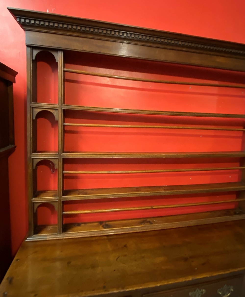 A George III oak dresser featuring an open upper plate rack with slender horizontal rails above three drawers and lower panelled cupboards with brass fittings. View VII