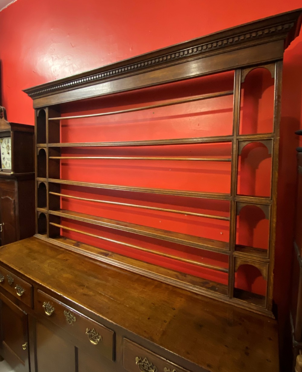 A George III oak dresser featuring an open upper plate rack with slender horizontal rails above three drawers and lower panelled cupboards with brass fittings. View VIII