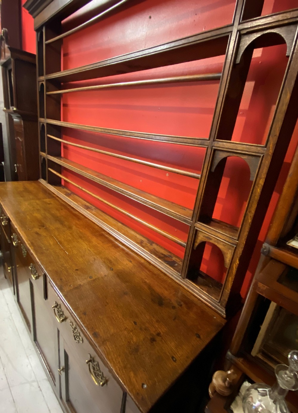 A George III oak dresser featuring an open upper plate rack with slender horizontal rails above three drawers and lower panelled cupboards with brass fittings. View IX