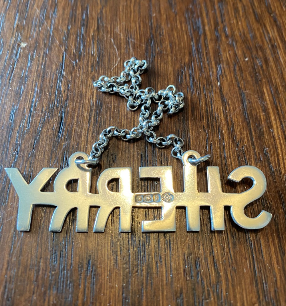 A solid silver decanter label formed from cut-out capital letters spelling SHERRY attached to a fine metal chain. View II
