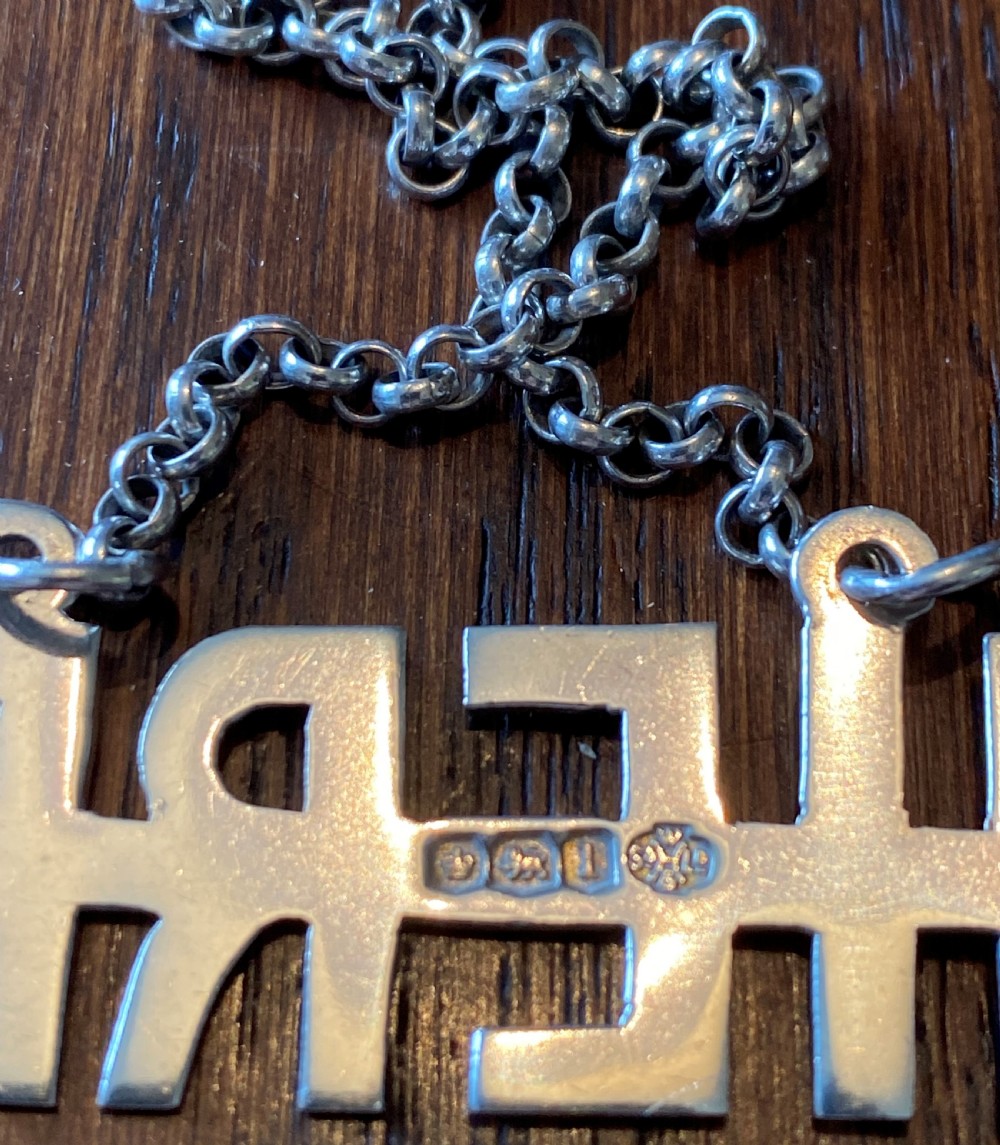 A solid silver decanter label formed from cut-out capital letters spelling SHERRY attached to a fine metal chain. View III