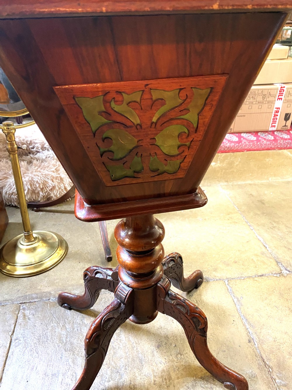 A Victorian walnut sewing table featuring a hinged lid decorated with an oval floral marquetry inlay set upon a carved tripod pedestal base. View VI