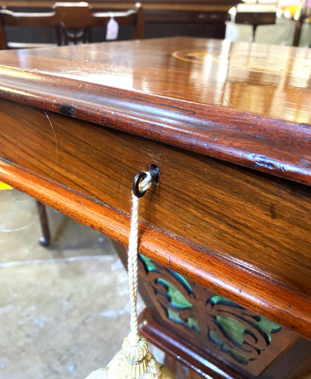 A Victorian walnut sewing table featuring a hinged lid decorated with an oval floral marquetry inlay set upon a carved tripod pedestal base. View IX