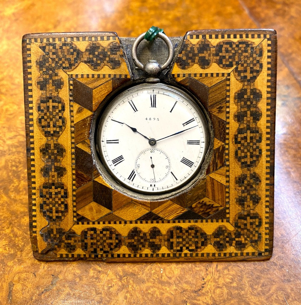 A square Victorian Tunbridge ware wooden pocket watch stand featuring geometric mosaic parquetry around a central pocket watch.