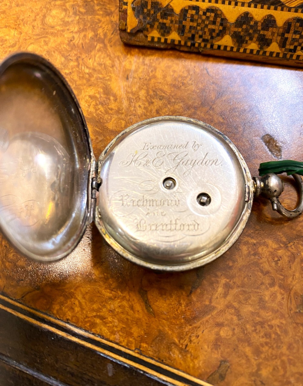 A square Victorian Tunbridge ware wooden pocket watch stand featuring geometric mosaic parquetry around a central pocket watch. View V