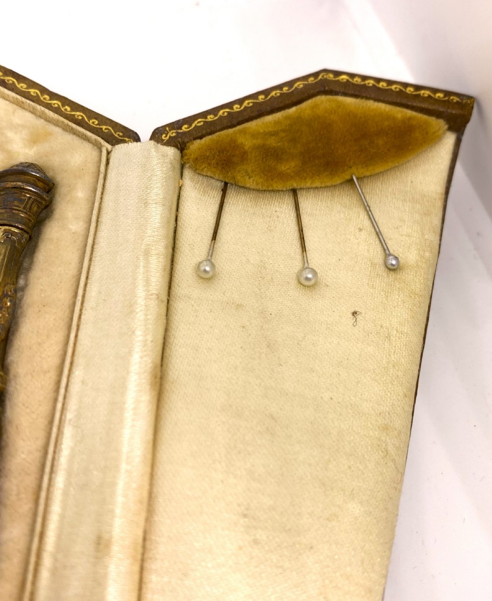 A tri-fold brown leather sewing etui open to display a cream silk interior holding gilt brass scissors, a thimble, and needlework tools. View IV