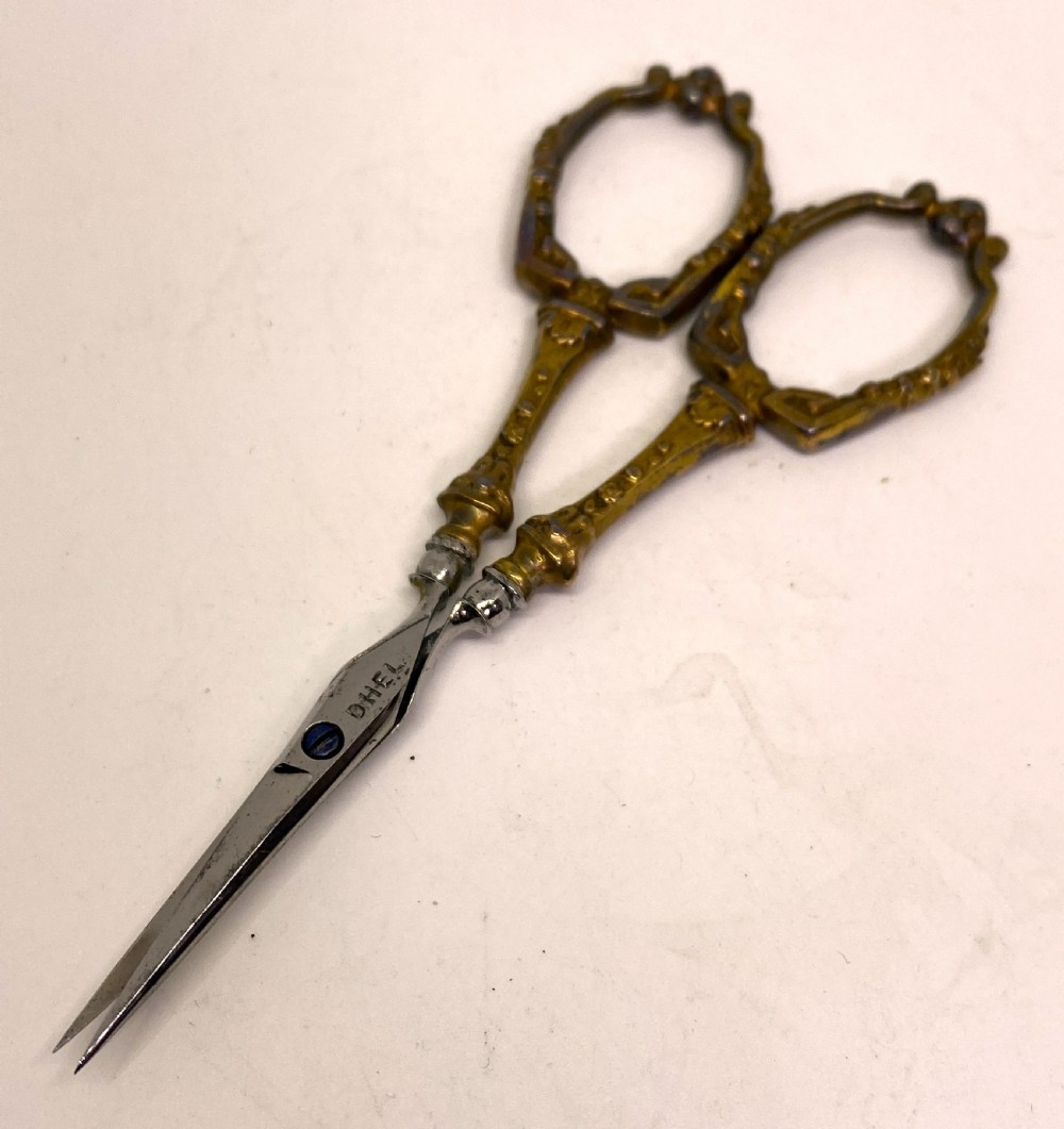 A tri-fold brown leather sewing etui open to display a cream silk interior holding gilt brass scissors, a thimble, and needlework tools. View V