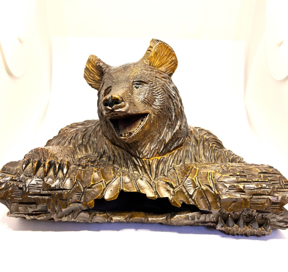 A hand-carved dark wood inkwell formed as a bear leaning over a hollow log.