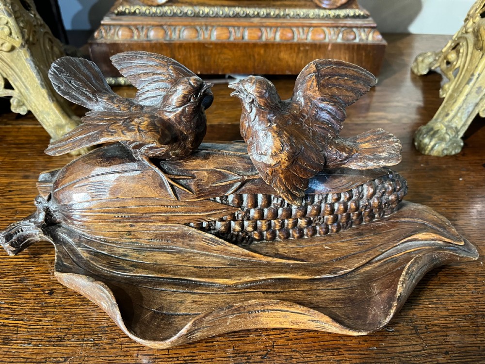 A dark hand-carved wooden double inkwell featuring two birds perched on a ear of corn with an integrated pen tray base.