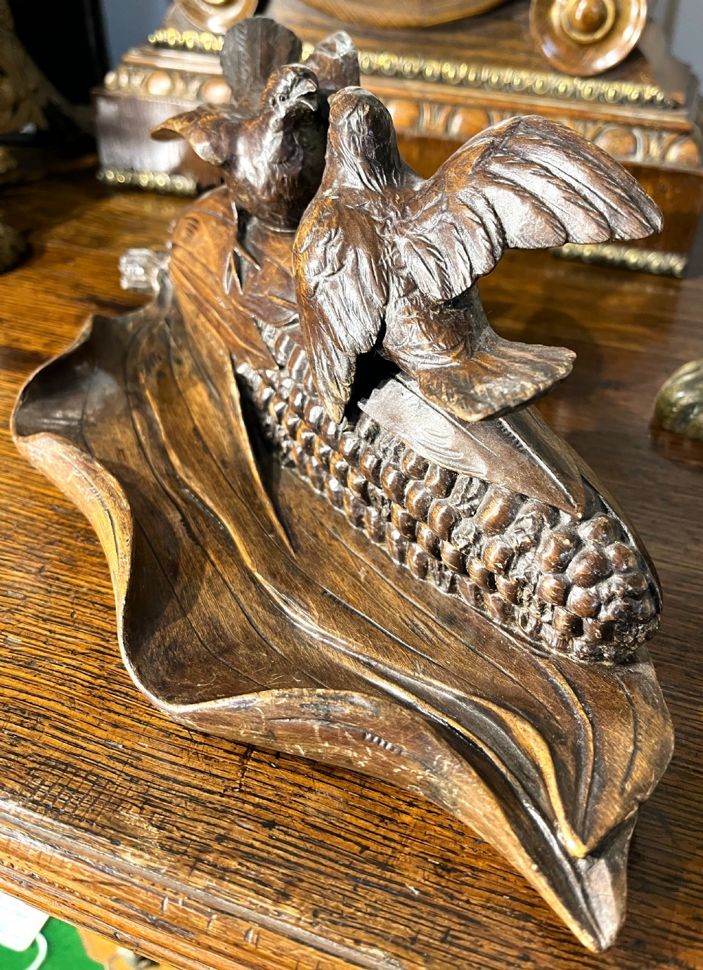 A dark hand-carved wooden double inkwell featuring two birds perched on a ear of corn with an integrated pen tray base. View VI