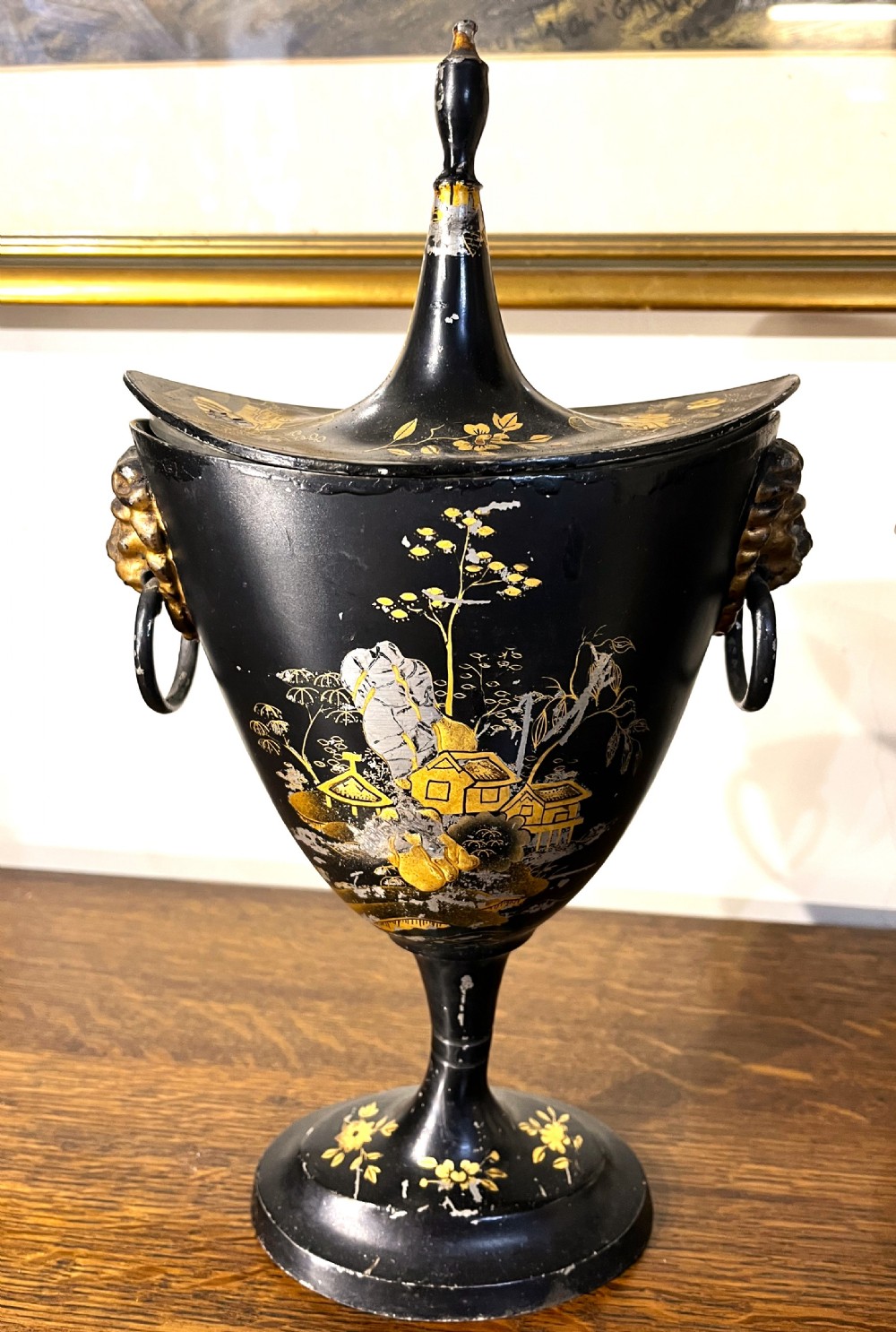 A pair of black painted metal toleware chestnut urns decorated with gold chinoiserie landscape scenes, pointed lids, and lion mask side handles. View II
