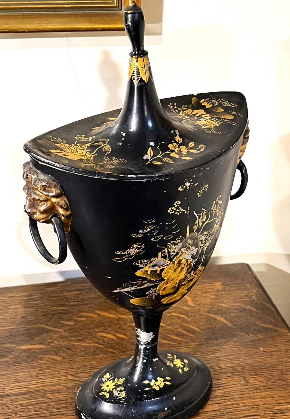 A pair of black painted metal toleware chestnut urns decorated with gold chinoiserie landscape scenes, pointed lids, and lion mask side handles. View V
