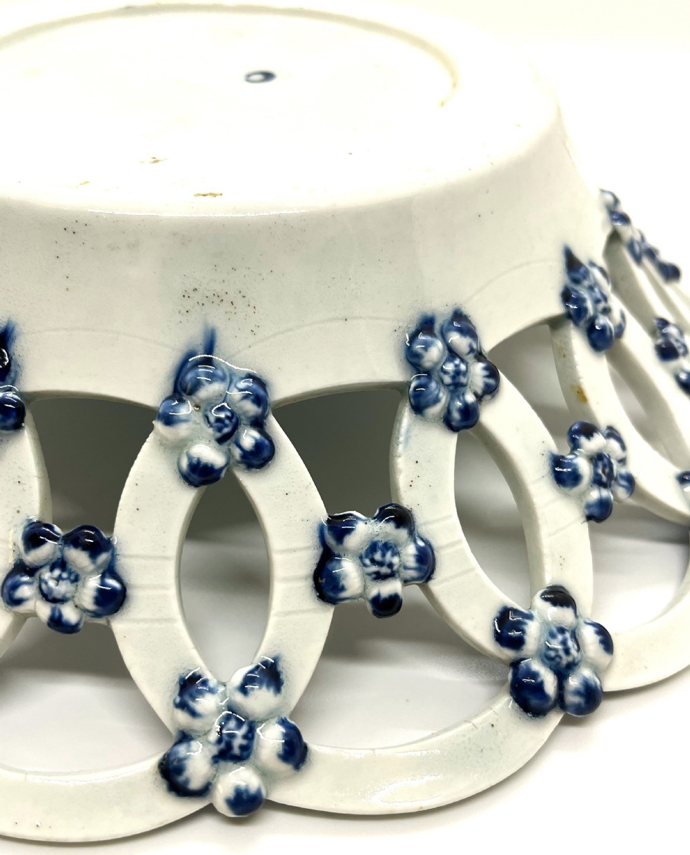 An 18th-century First Period Worcester circular soft-paste porcelain basket featuring a reticulated lattice rim and blue and white transfer-printed pinecone pattern. View VI