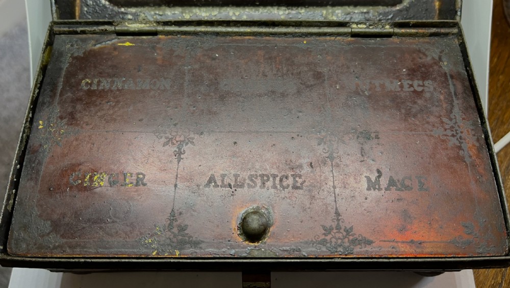 An open black lacquered toleware spice box displaying labelled inner compartments and a nutmeg grater fitted inside the lid. View IV