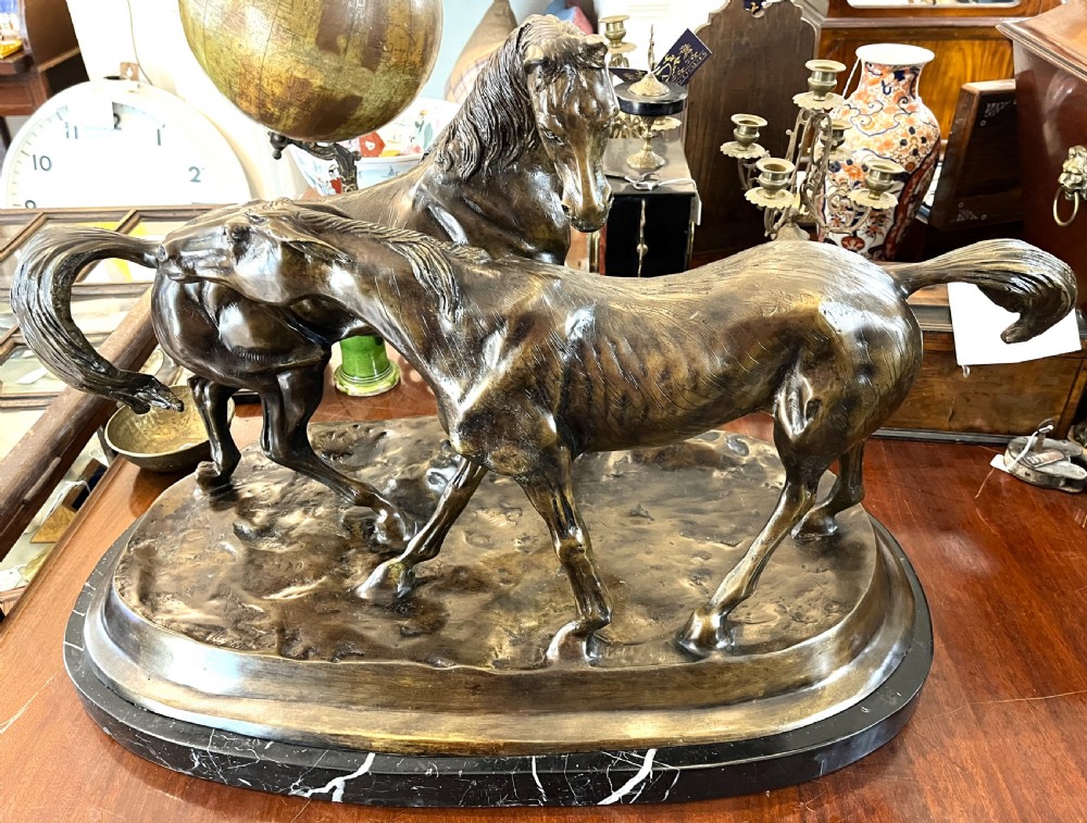 A bronze sculpture depicting two horses standing together on a naturalistic ground base mounted on an oval dark marble plinth. View II