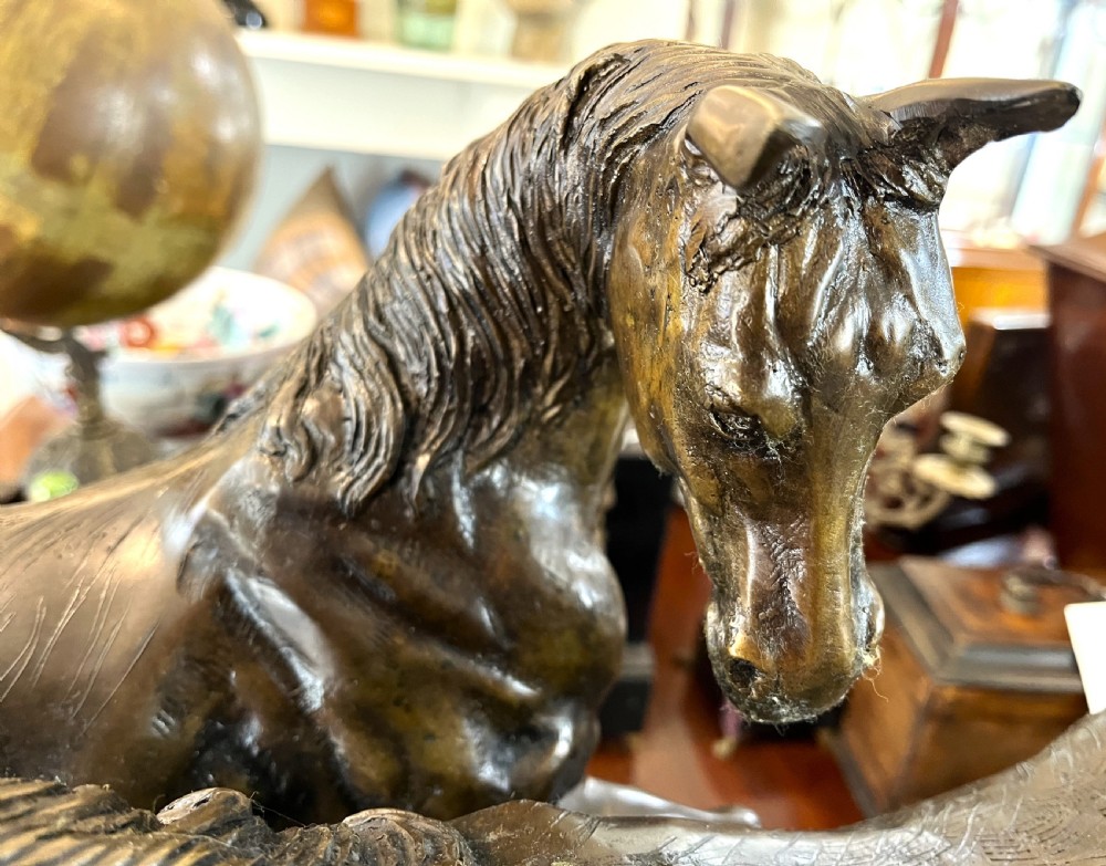 A bronze sculpture depicting two horses standing together on a naturalistic ground base mounted on an oval dark marble plinth. View IV