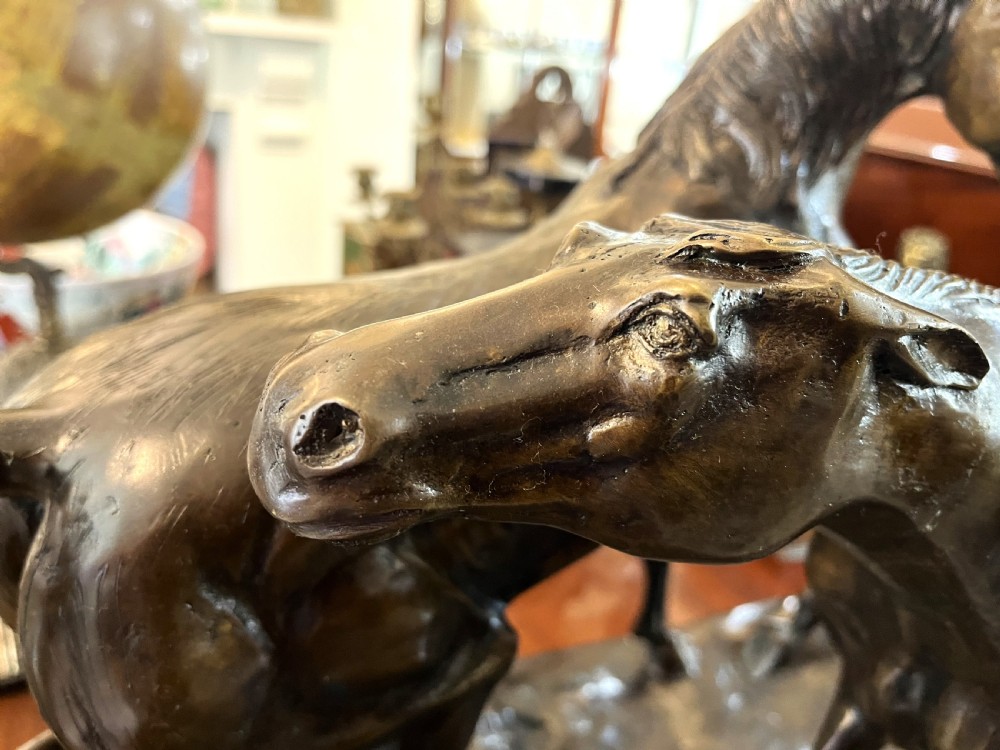 A bronze sculpture depicting two horses standing together on a naturalistic ground base mounted on an oval dark marble plinth. View VI