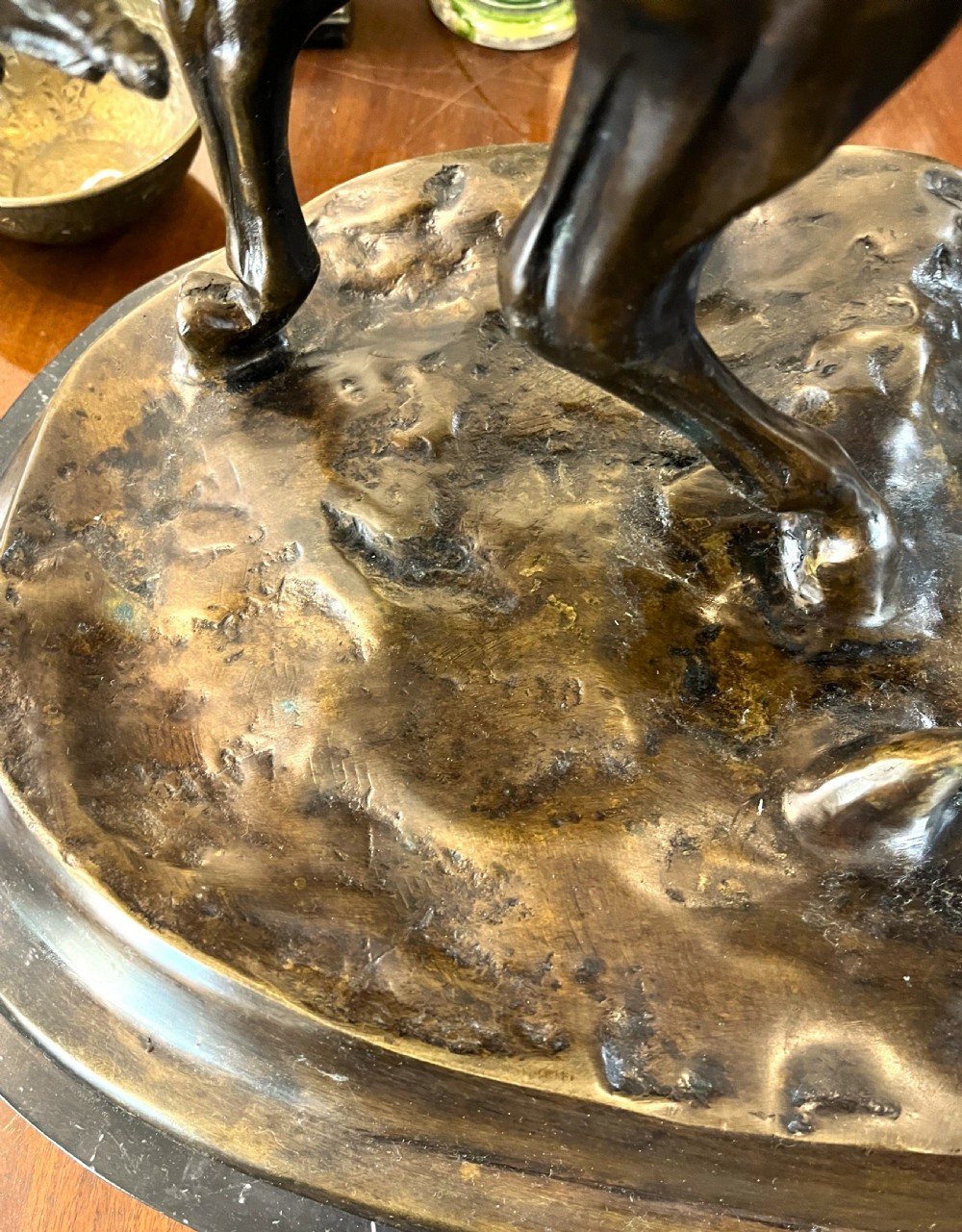A bronze sculpture depicting two horses standing together on a naturalistic ground base mounted on an oval dark marble plinth. View VII