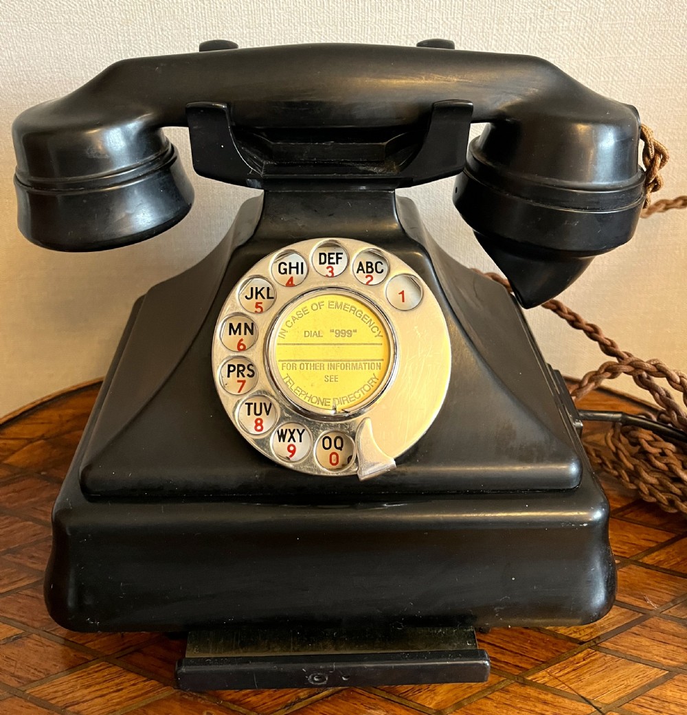 A black Bakelite rotary telephone from the 1930s featuring a central metal dial with red and black lettering.