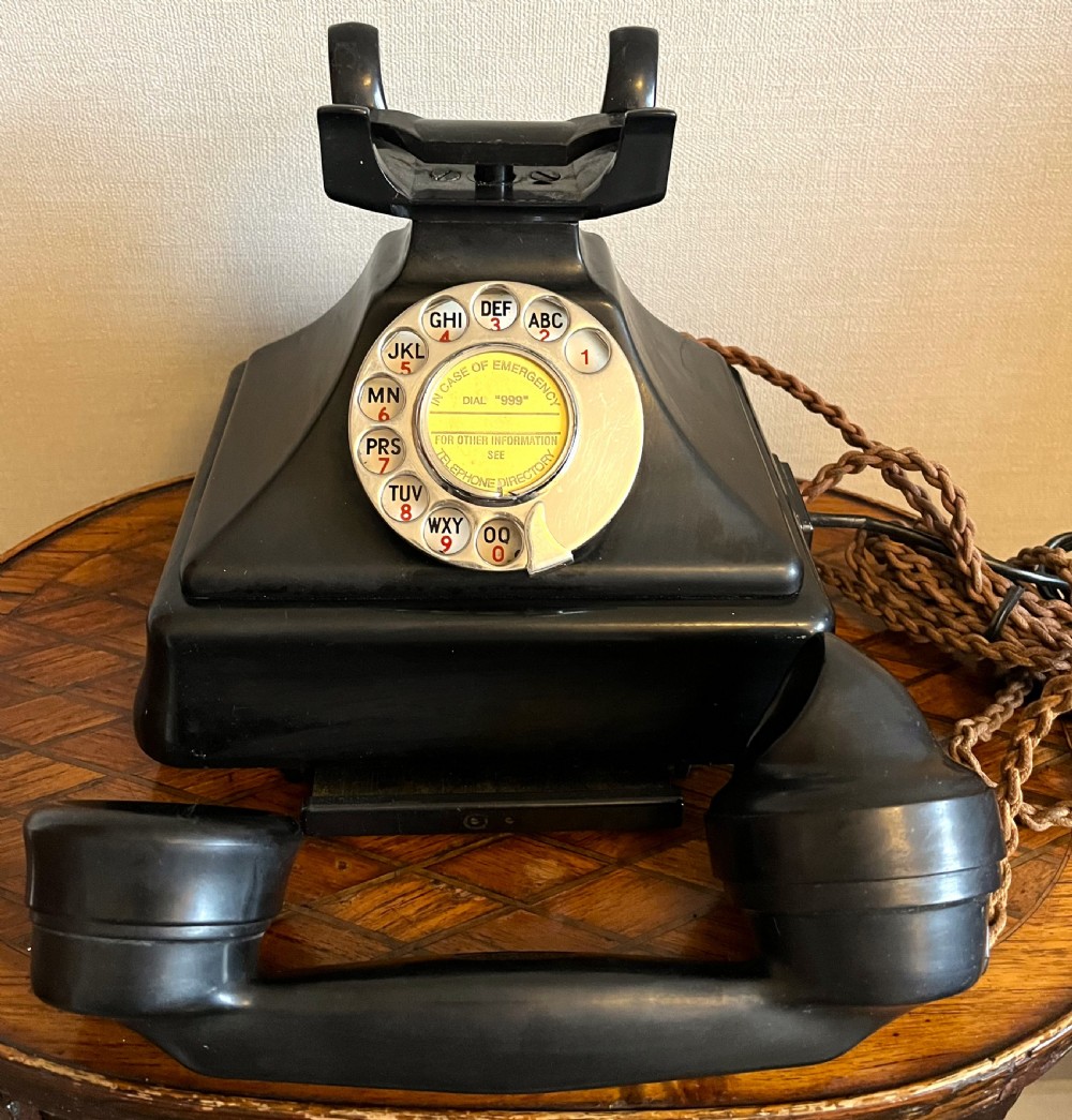 A black Bakelite rotary telephone from the 1930s featuring a central metal dial with red and black lettering. View II