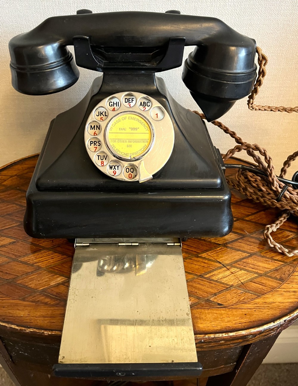 A black Bakelite rotary telephone from the 1930s featuring a central metal dial with red and black lettering. View III