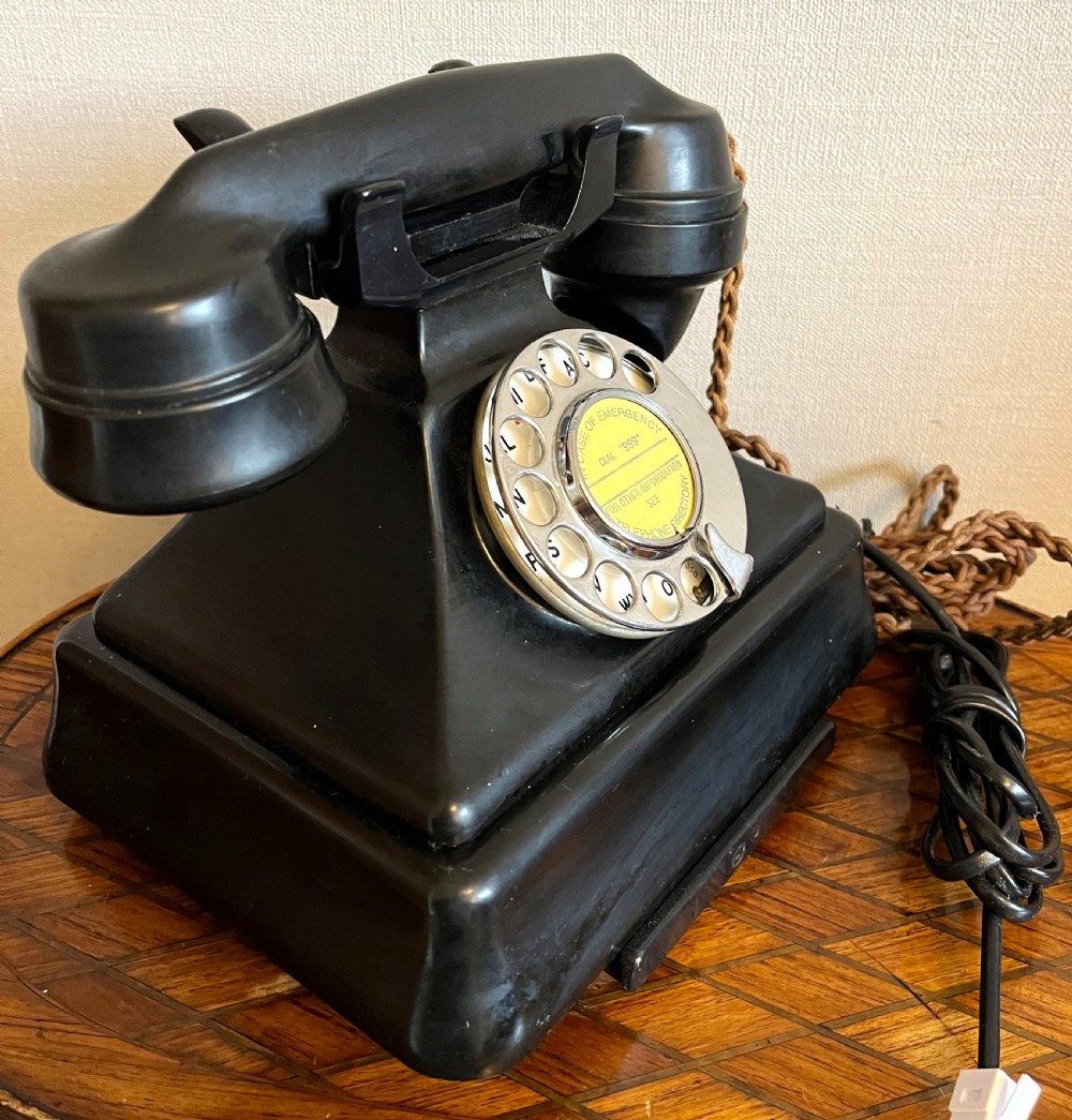 A black Bakelite rotary telephone from the 1930s featuring a central metal dial with red and black lettering. View IV