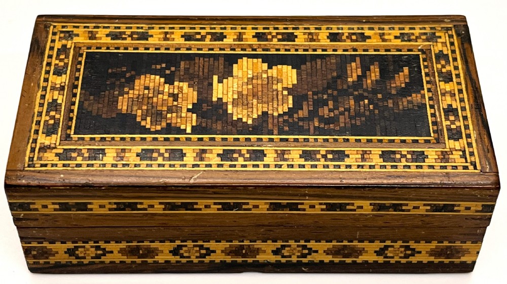 A rectangular dark wood box featuring an intricate tessellated mosaic floral design on the lid framed by geometric inlaid borders.