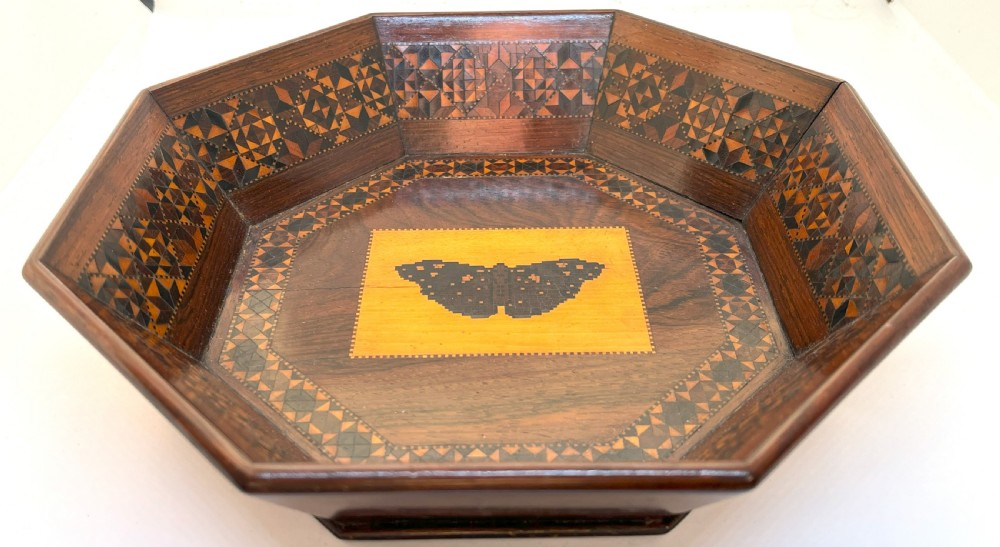 An octagonal Victorian Tunbridge ware wooden dish featuring geometric mosaic borders and a central yellow wooden panel with a black butterfly inlay.