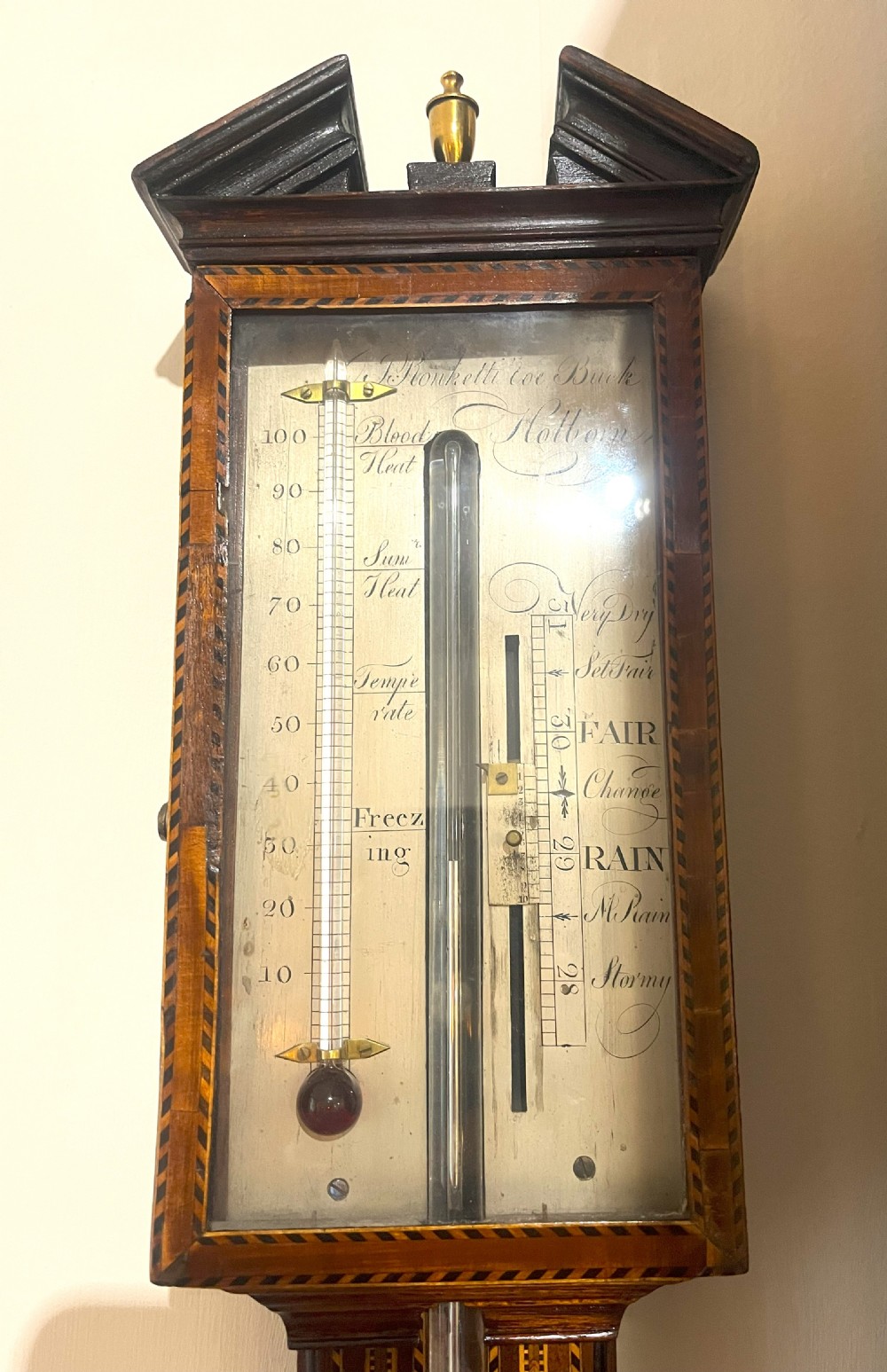 An antique Georgian mahogany stick barometer featuring geometric parquetry inlay, a broken pediment top, and an engraved silvered register plate. View VI