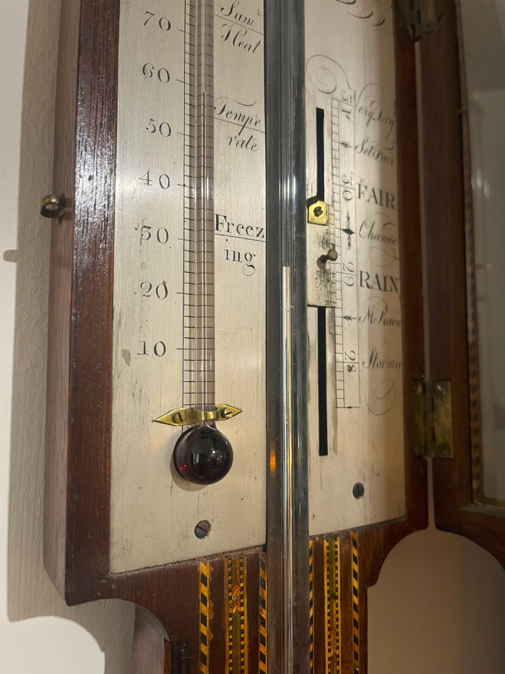 An antique Georgian mahogany stick barometer featuring geometric parquetry inlay, a broken pediment top, and an engraved silvered register plate. View VII