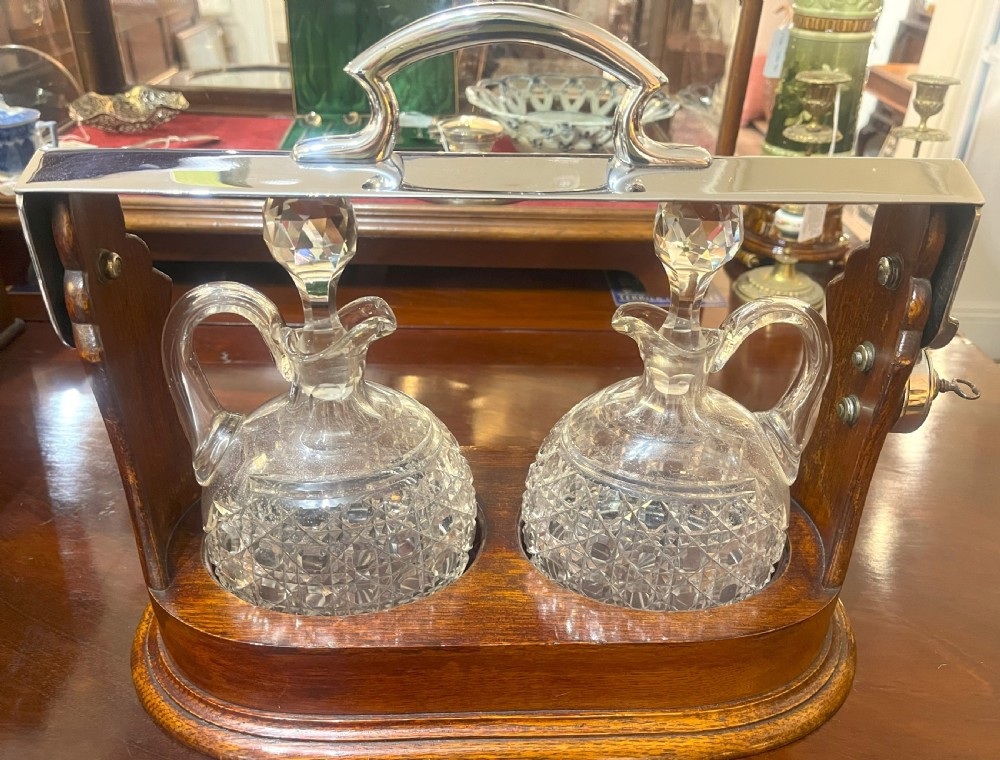 An Edwardian wooden tantalus housing two cut crystal jugs with stoppers under a silver-plated locking top bar.