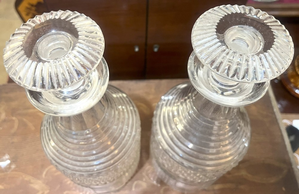 A pair of Georgian clear cut crystal decanters featuring diamond cut bands, ringed necks, and matching glass stoppers. View II
