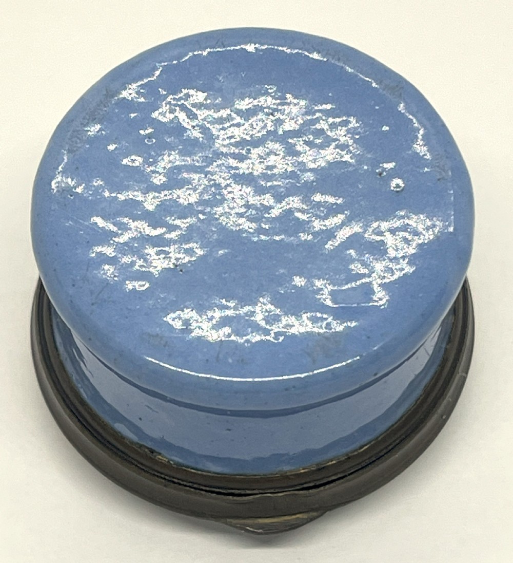 A circular Georgian South Staffordshire enamel patch box featuring a light blue base and a hinged lid adorned with a white bird motif on a navy blue ground. View IV