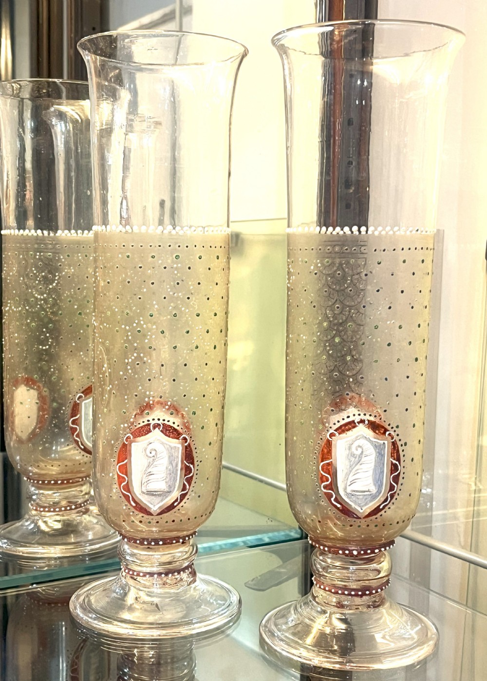 A pair of tall clear glass vases featuring hand-painted white and red enamel dot patterning and heraldic shield crests on stepped pedestal bases.