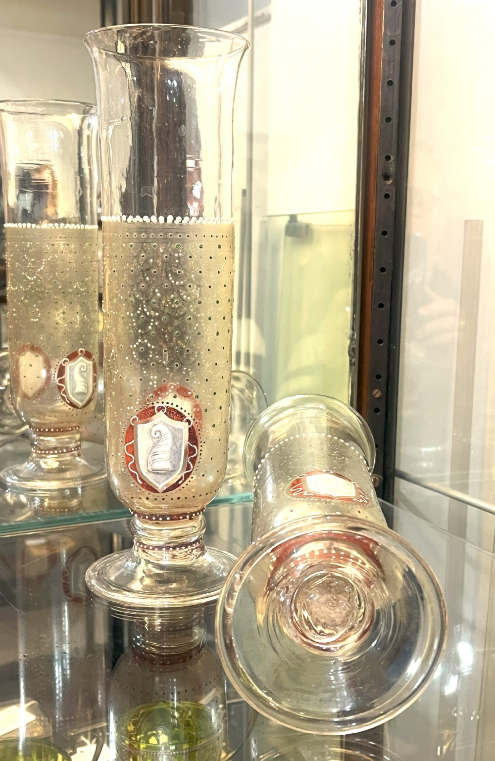 A pair of tall clear glass vases featuring hand-painted white and red enamel dot patterning and heraldic shield crests on stepped pedestal bases. View V