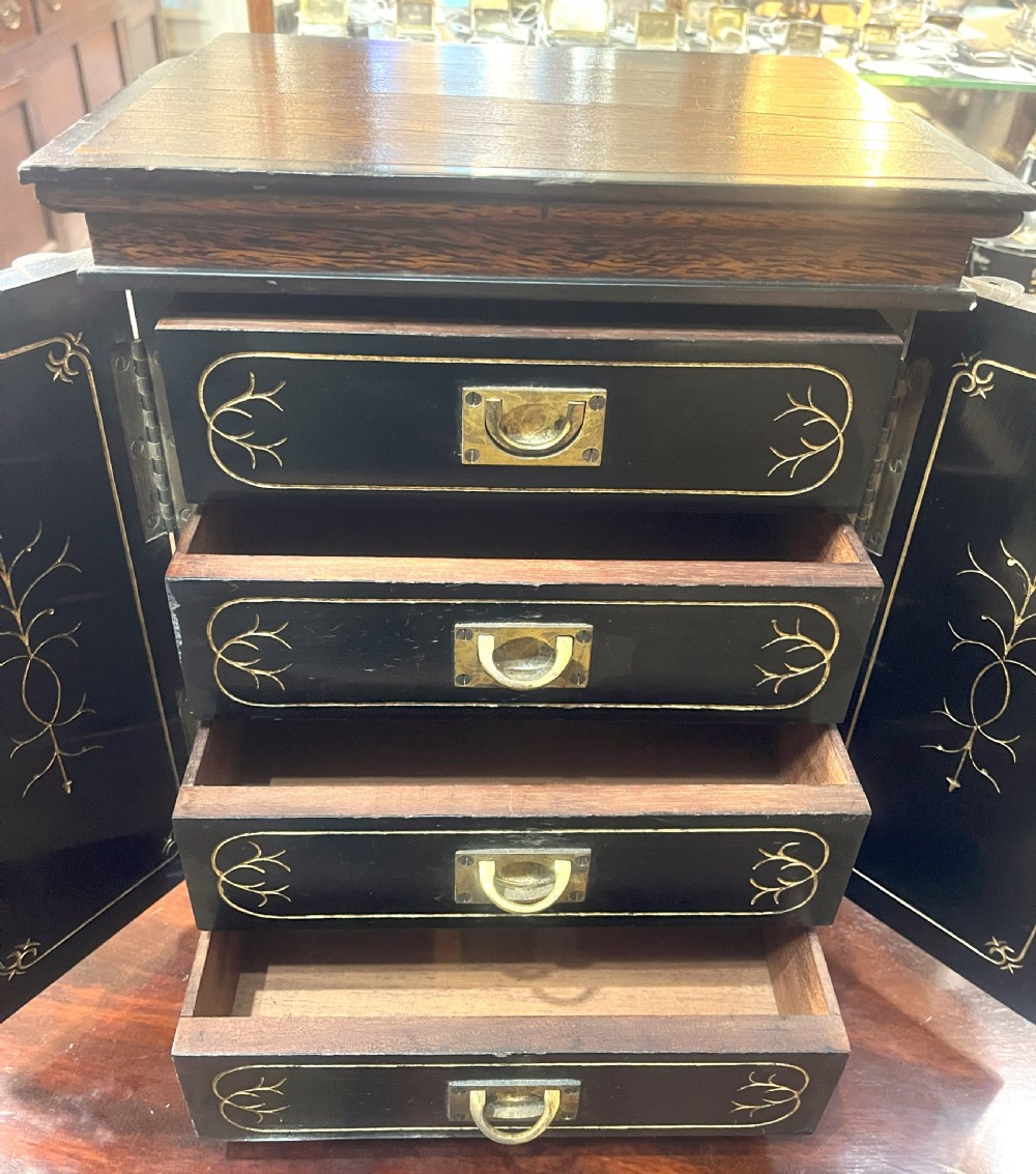 A nineteenth-century ebonised palmwood table cabinet with opened double doors revealing four small drawers with flush brass handles and gold foliate decoration. View II