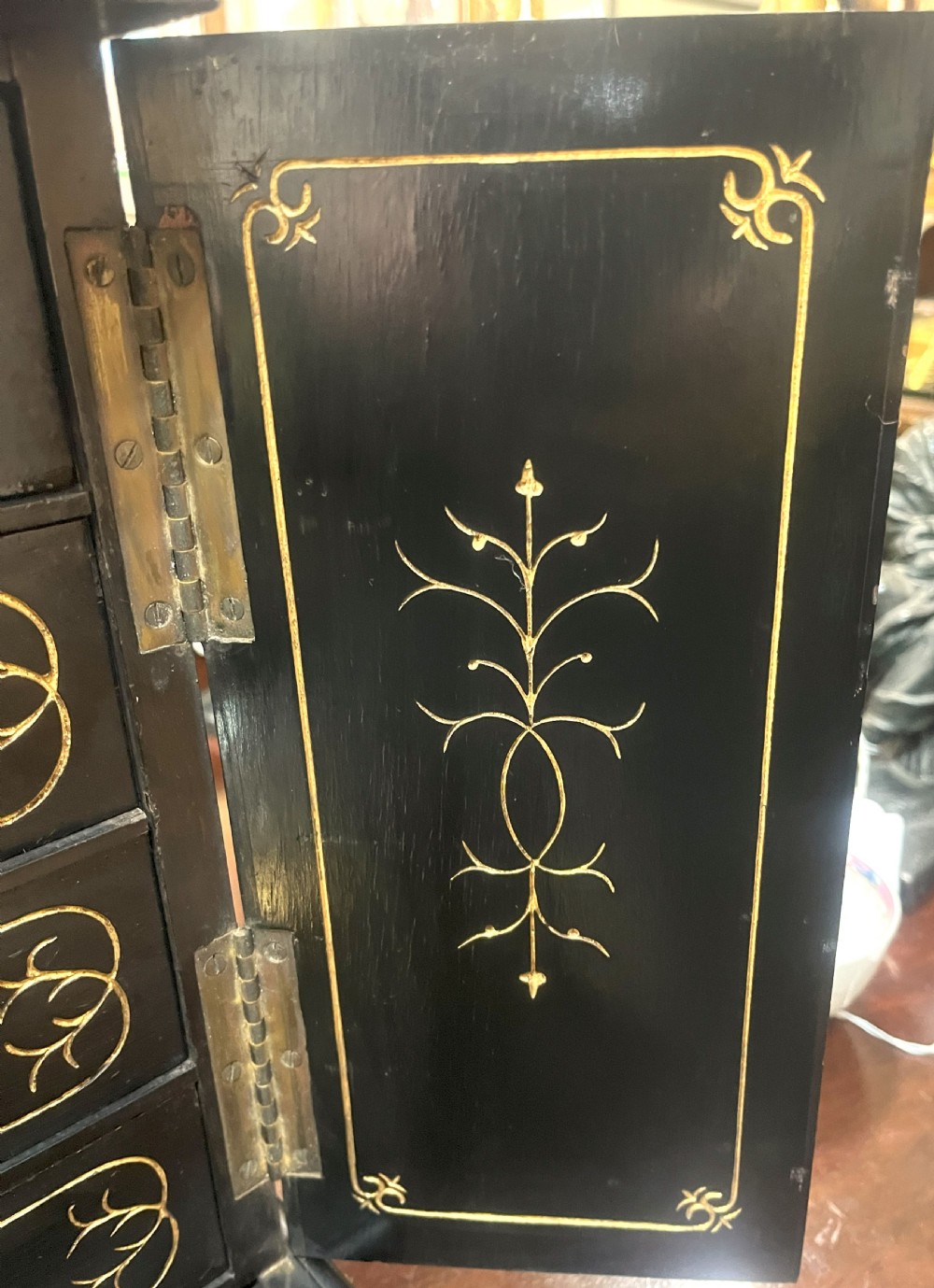 A nineteenth-century ebonised palmwood table cabinet with opened double doors revealing four small drawers with flush brass handles and gold foliate decoration. View IV
