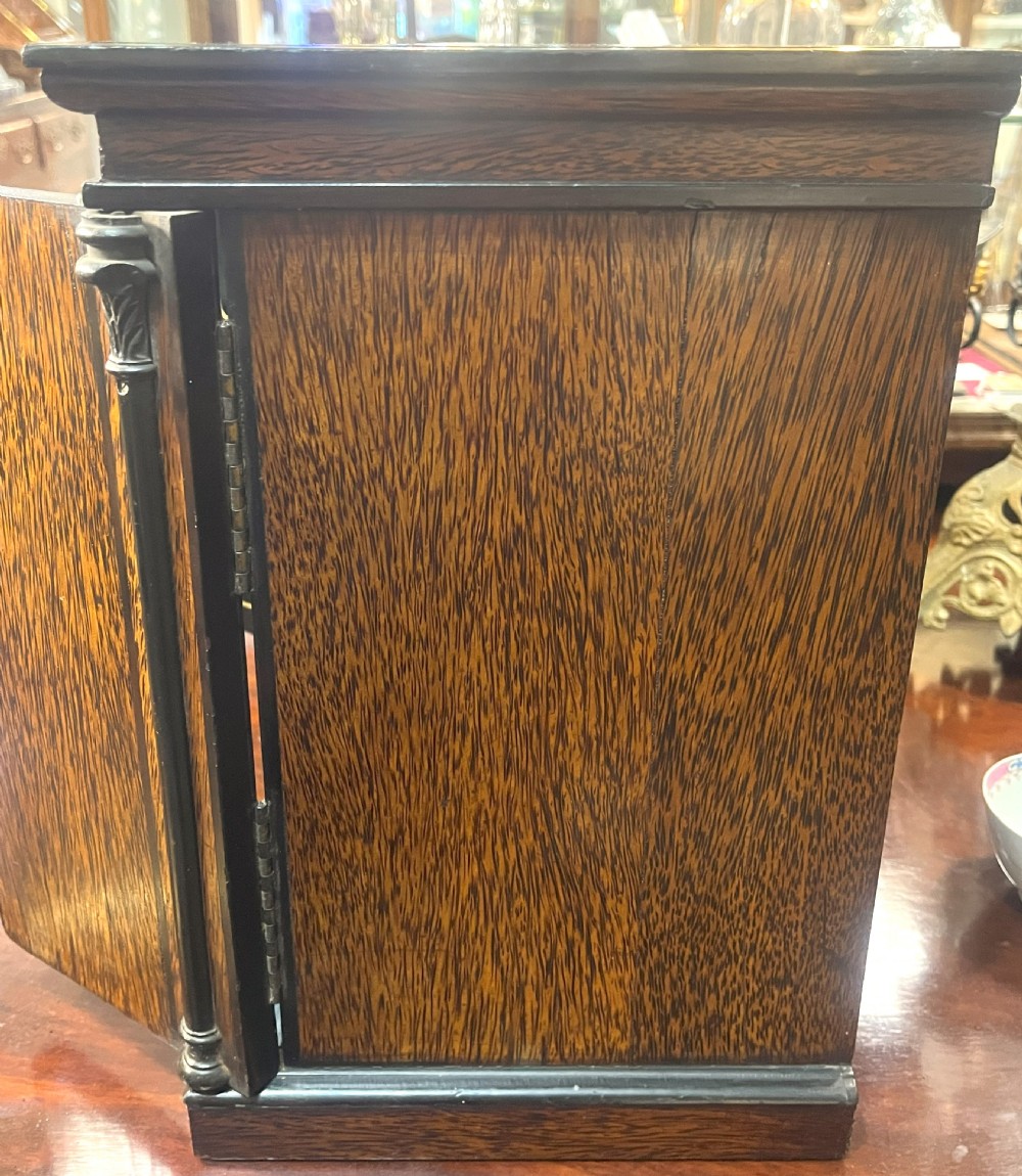 A nineteenth-century ebonised palmwood table cabinet with opened double doors revealing four small drawers with flush brass handles and gold foliate decoration. View VI