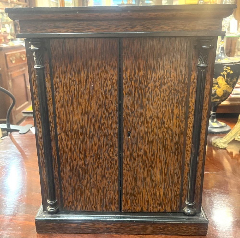 A nineteenth-century ebonised palmwood table cabinet with opened double doors revealing four small drawers with flush brass handles and gold foliate decoration. View VIII